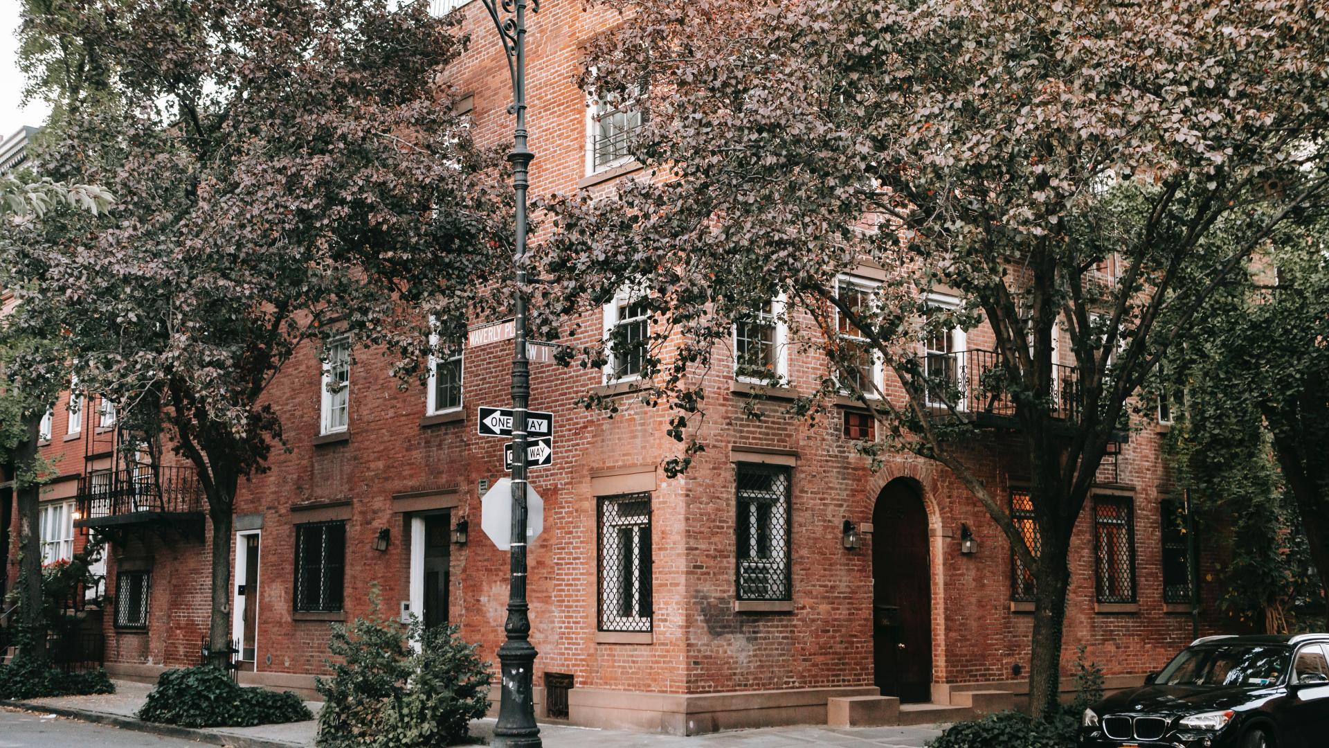 Red brick building on the corner of the street with trees in front of it