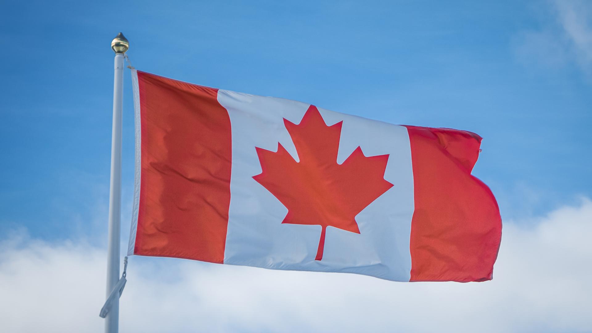 Canada flag open at the top of the pole with a blue sky background