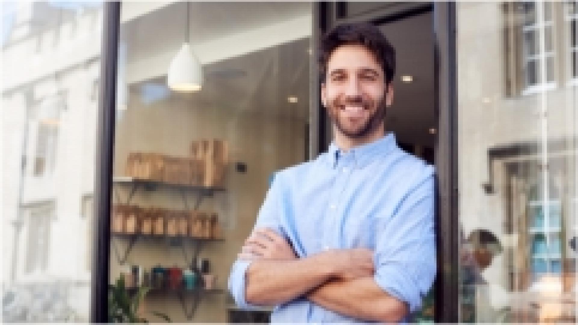 Man in a blue collared button up shirt leaning against the doorway of a shop