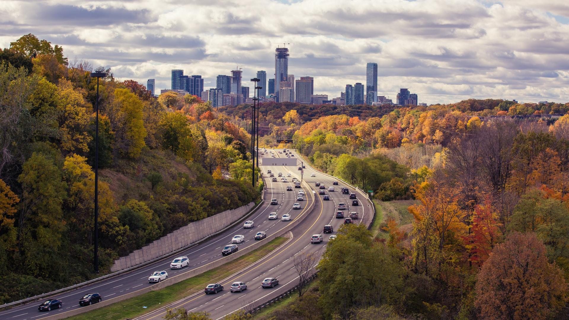 A highway with cars on it and trees with a city in the background