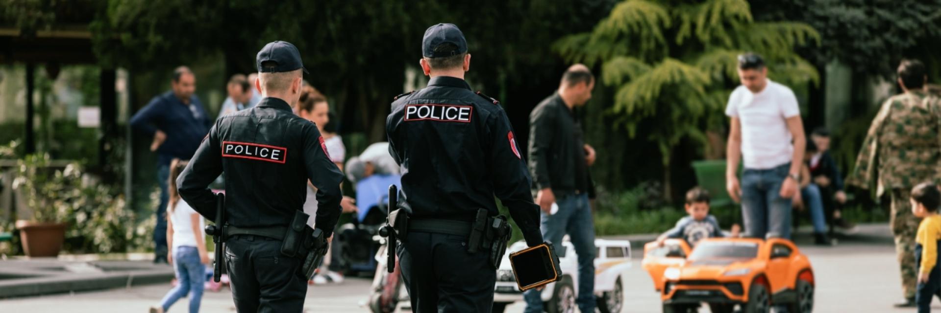 Two police officers walking away from the camera past a group of citizens playing with their children