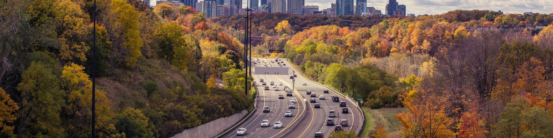 A highway with cars on it and trees with a city in the background