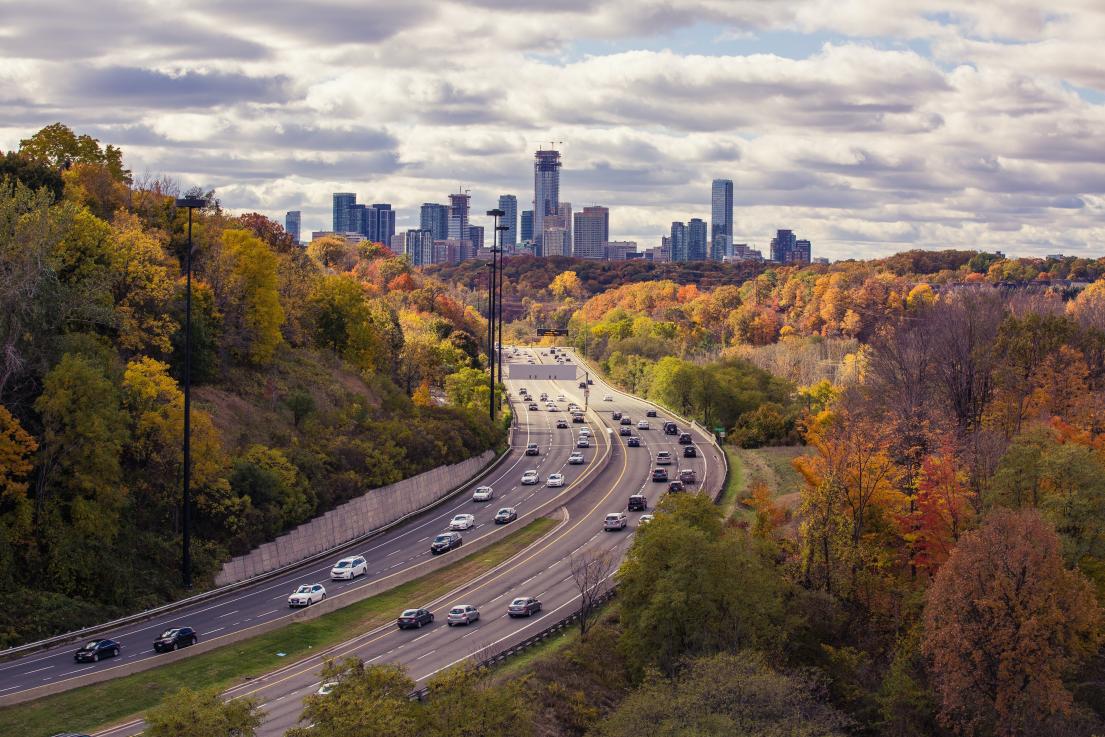 A highway with cars on it and trees with a city in the background